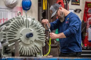 Technician working on industrial equipment, wearing safety glasses and a Southwest Electric Co. branded shirt, with a motor in the foreground.