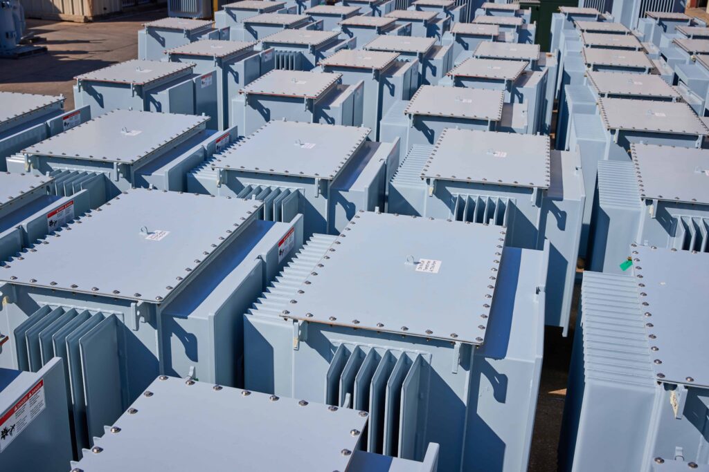 A large number of light blue industrial transformers neatly arranged outdoors, awaiting installation or distribution.